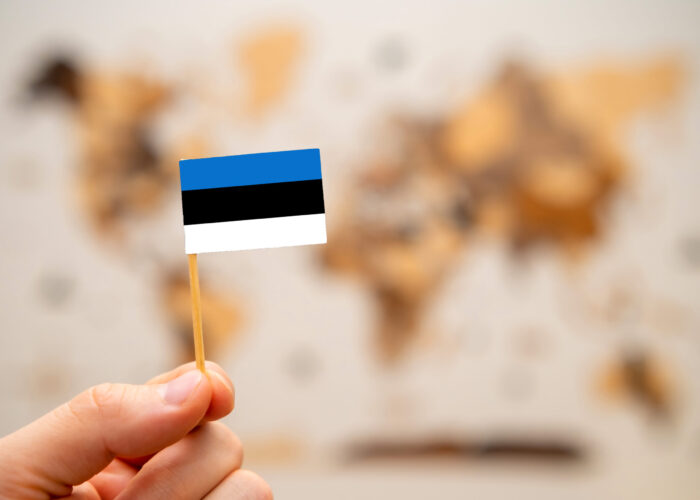 Estonia flag in mans hand on the world map background. Estonia flag in mans hand on the wooden world map background. Global economy and geopolitics concept.