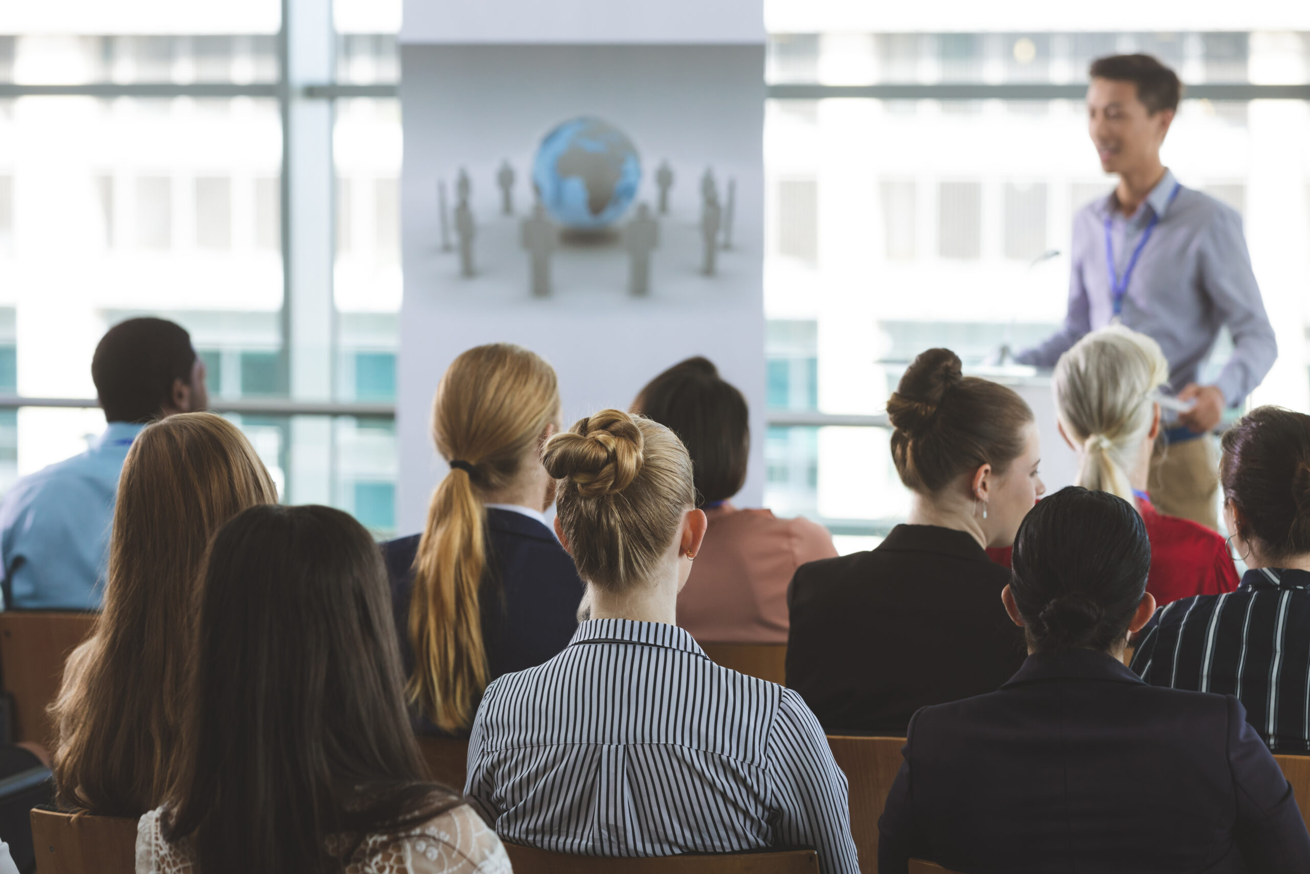 Rear view of diverse group of business professionals attending a seminar with an male Asian speaker in office building